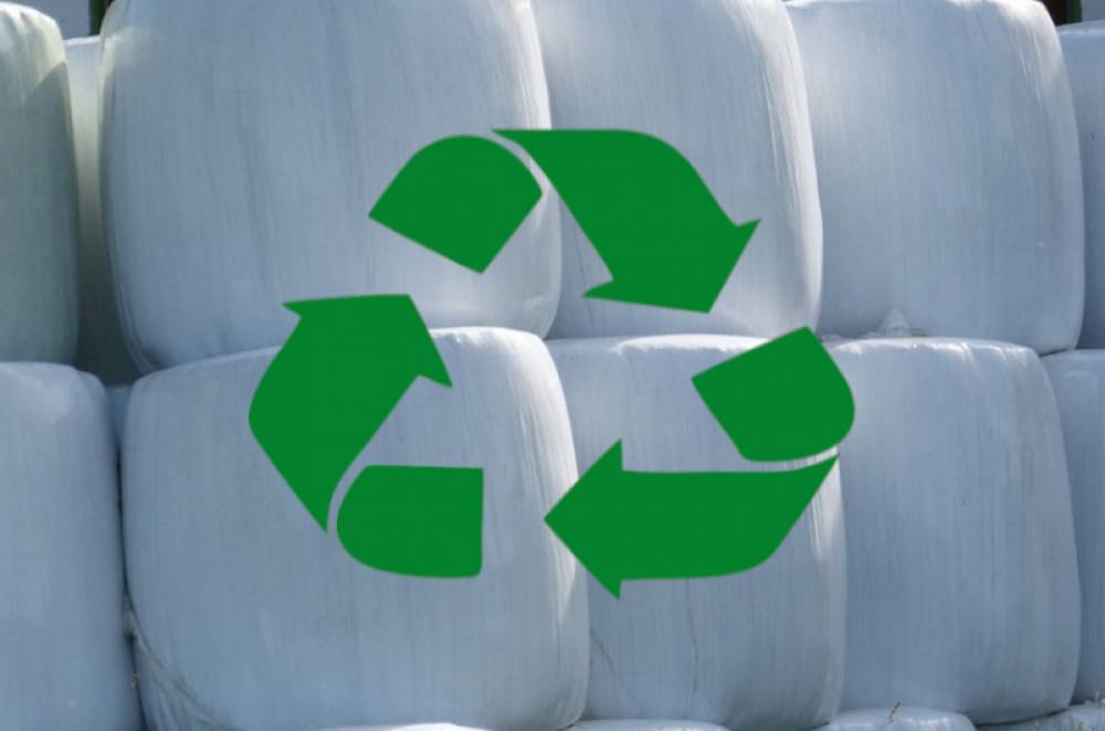 : Baloty owinięte białą folią, na środku zielony znak recyklingu.
